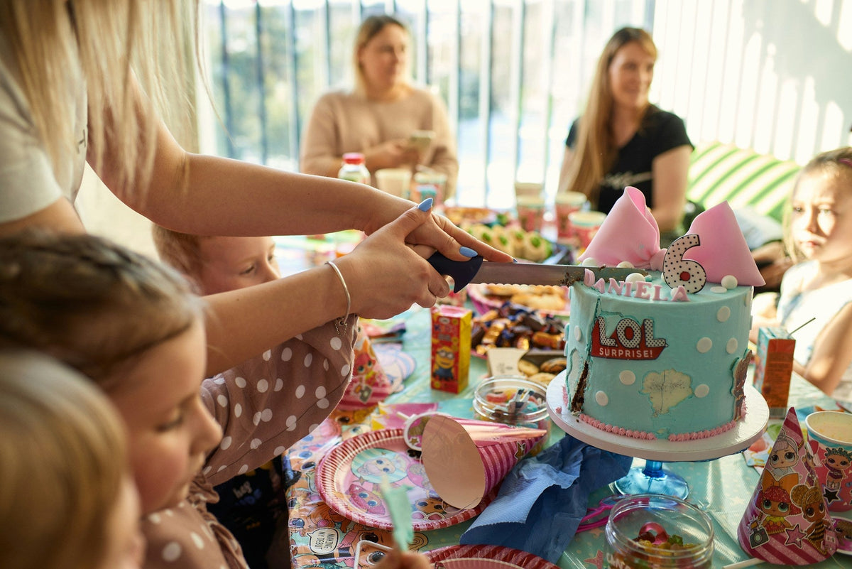 A woman is cutting a cake at a birthday party