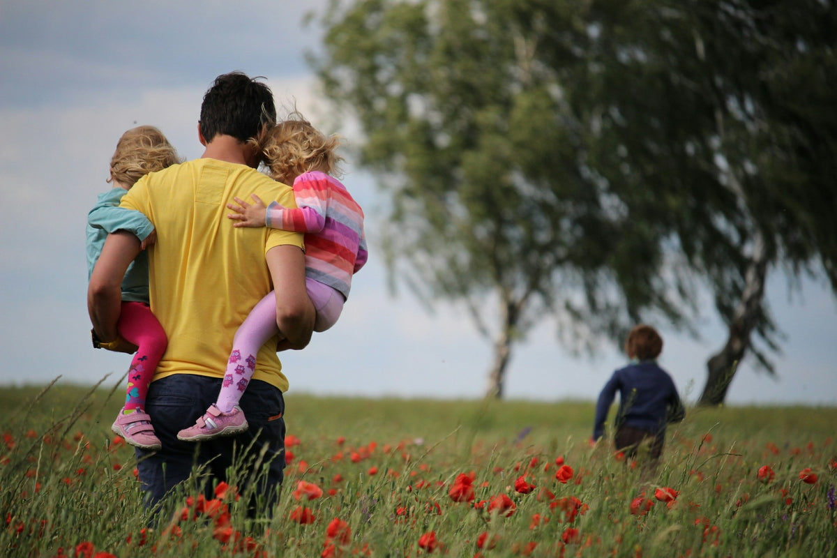 A man carrying two children through a field of flowers